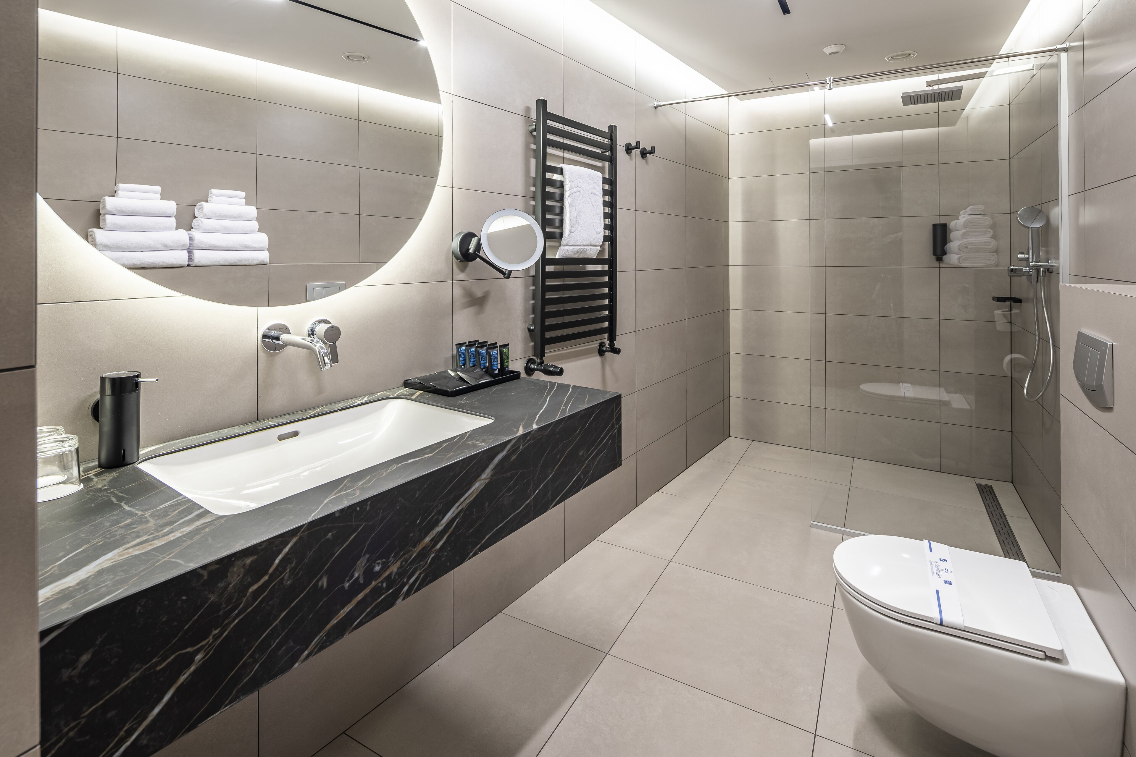 A modern bathroom with a large sink, mirror, towel rack, and a glass-enclosed shower area.