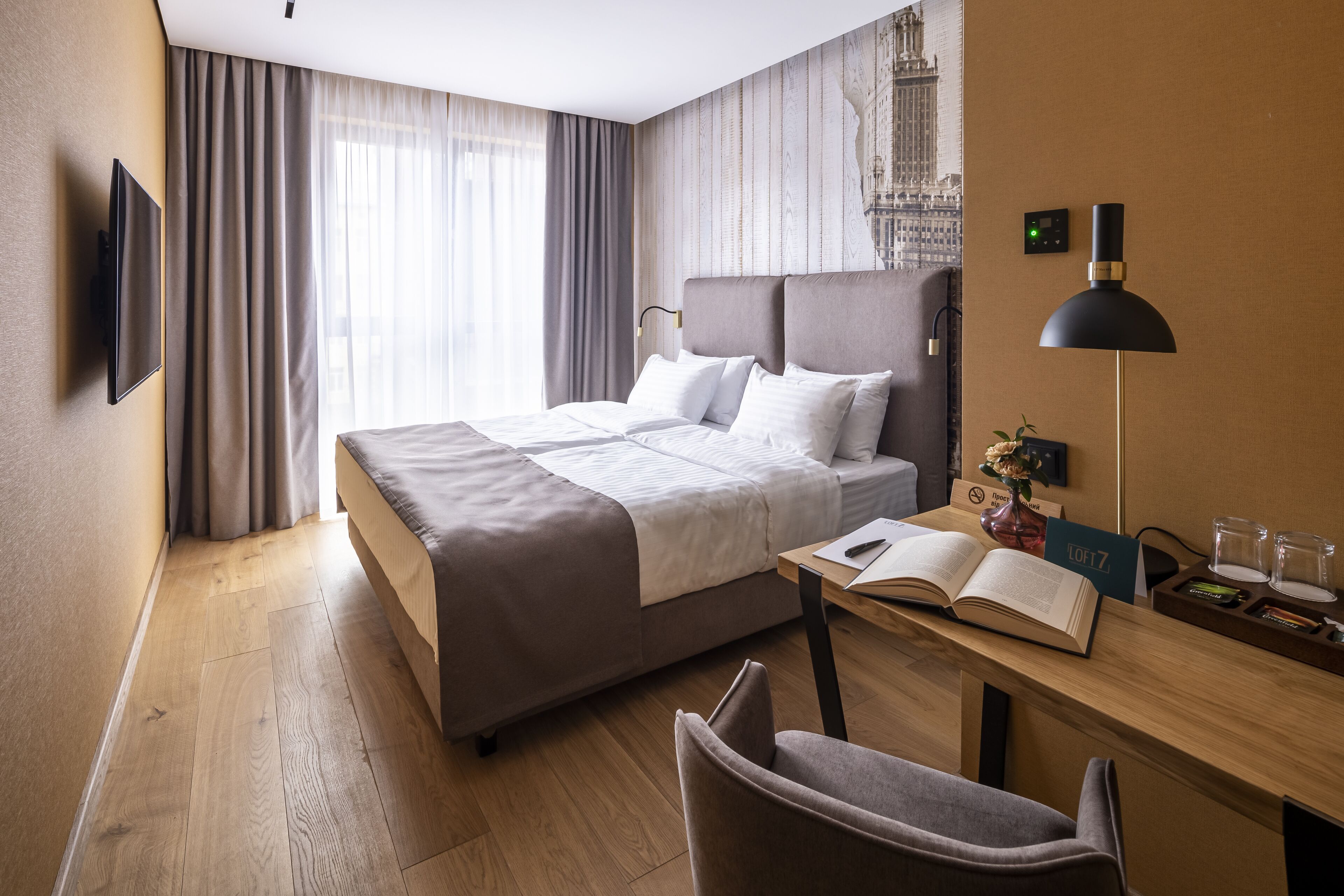 Une chambre d’hôtel avec un lit, un bureau, une chaise, une télévision et une fenêtre avec des rideaux.