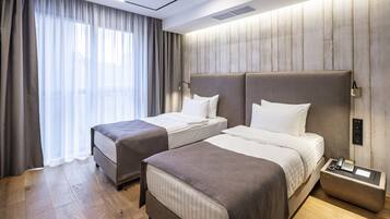 A hotel room with two beds, a bedside table with a phone, and a large window with curtains.
