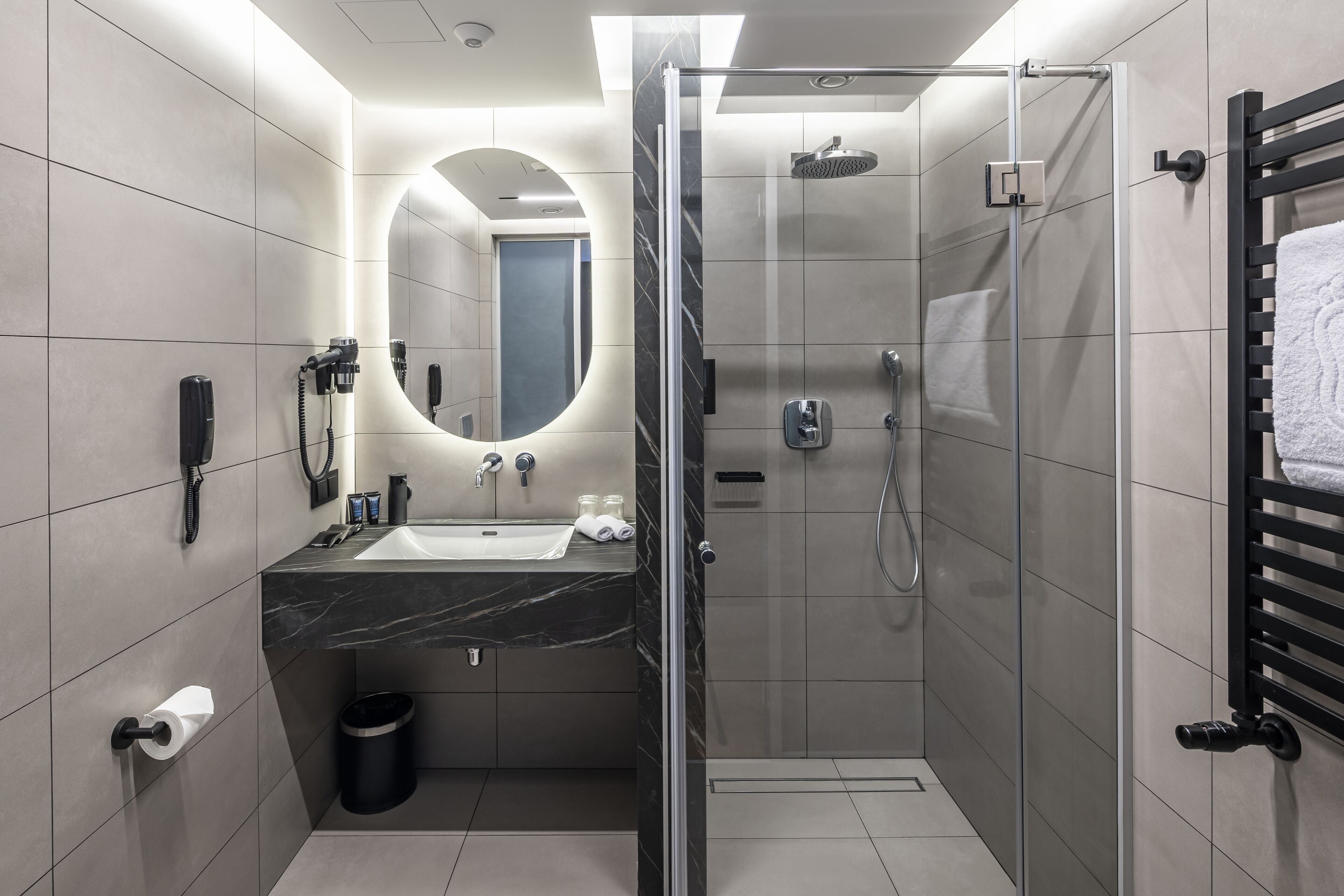 A modern bathroom with a glass-enclosed shower, a vanity with a marble countertop, and a large mirror.