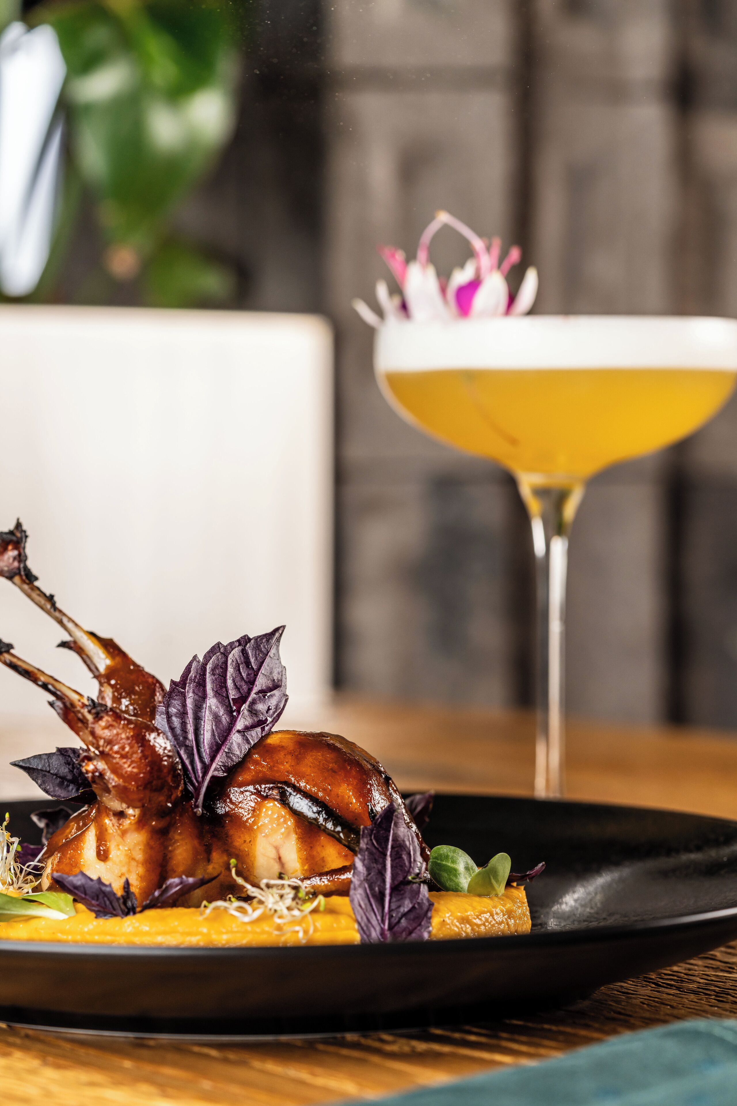 A plate with roasted duck and vegetables, and a cocktail glass in the background.