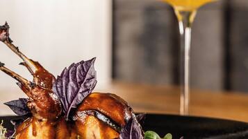 A plate with roasted duck and vegetables, and a cocktail glass in the background.