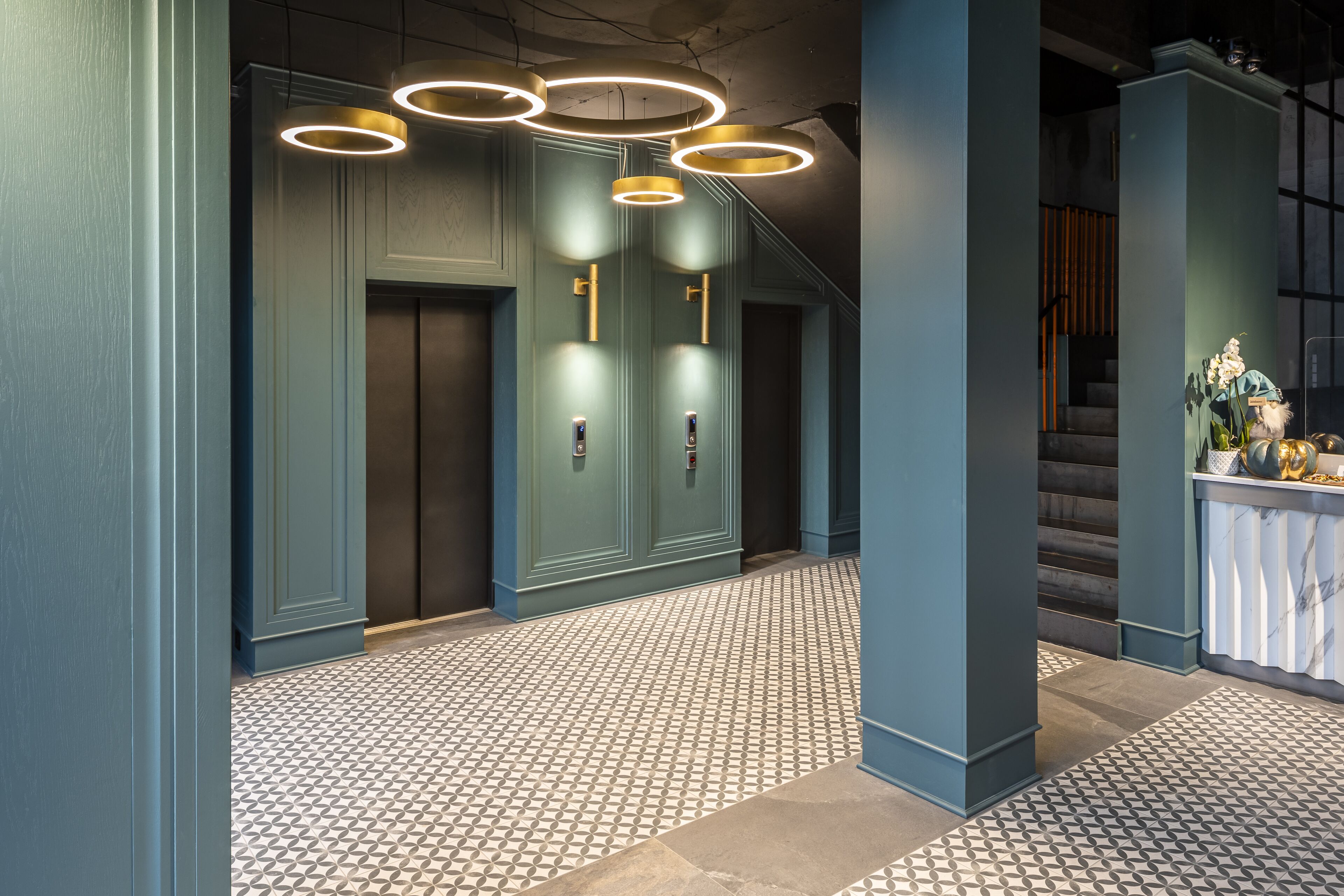 A modern lobby with a geometric patterned floor, a reception desk, and a staircase.