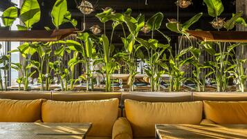 Un restaurante con techos altos, plantas colgantes y asientos acolchados amarillos.
