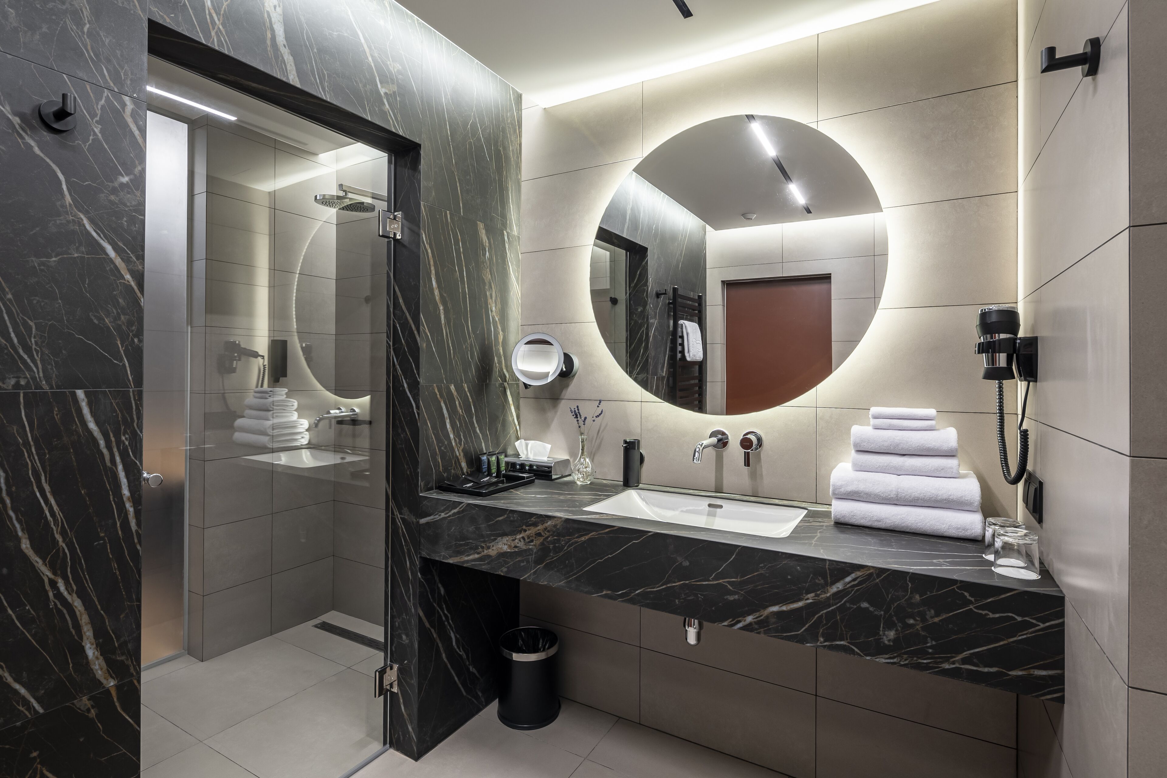 A modern bathroom with a marble vanity, a large mirror, and a glass shower enclosure.