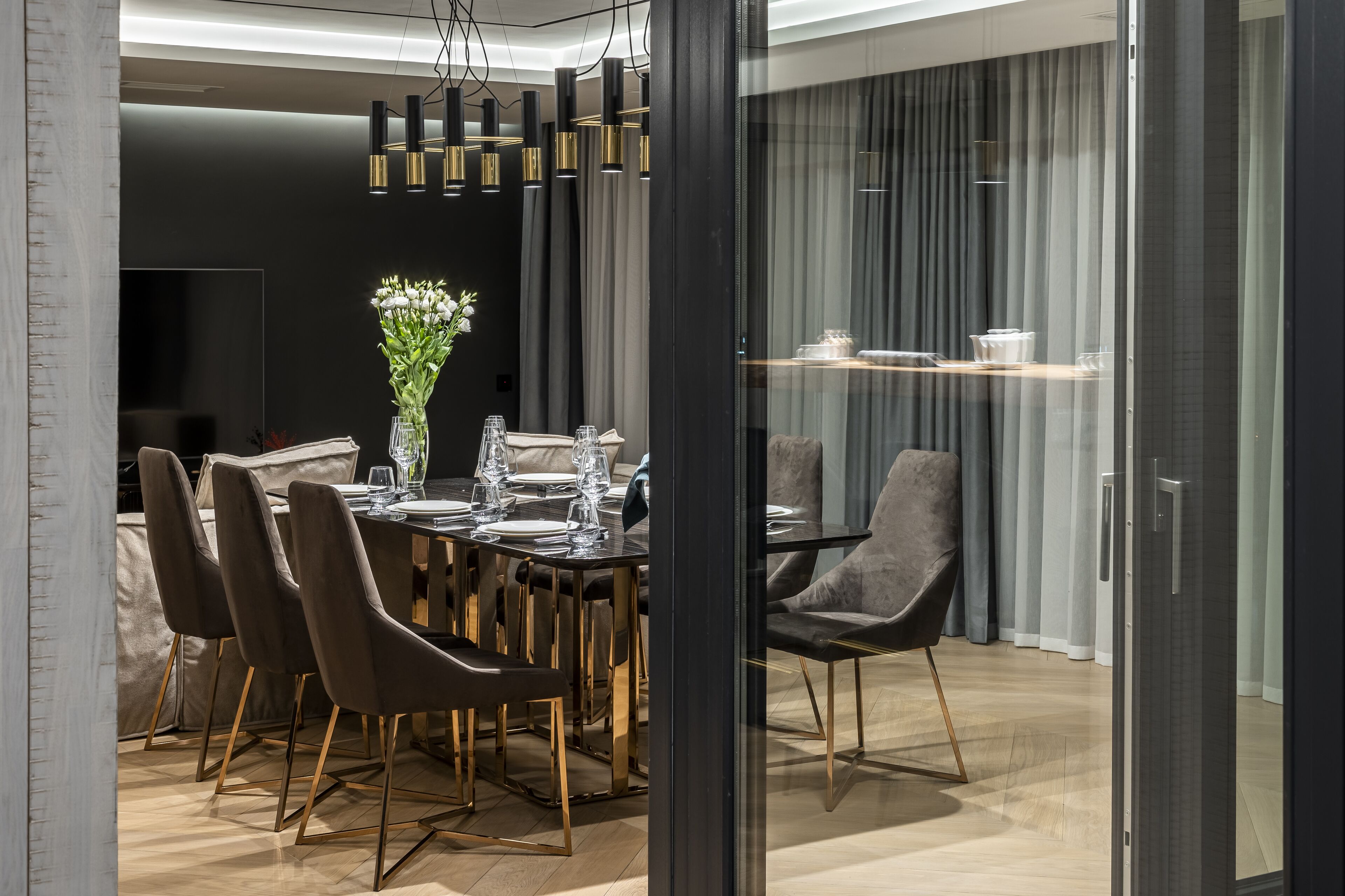 Un espace repas moderne avec une table en verre, des chaises foncées et un vase de fleurs.