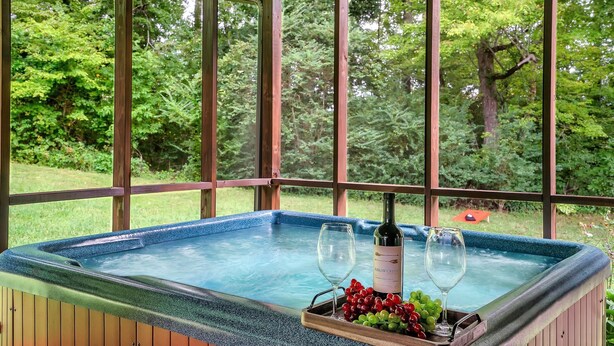 Ein Whirlpool mit einer Weinflasche und Trauben, umgeben von Holzverkleidungen und großen Fenstern.