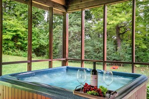 A hot tub with a bottle of wine and grapes, surrounded by wooden panels and large windows. - Fall Sale!Family Friendly/Large Yard/Hot Tub/Fire Pit/Game Room/Theater/Pets (Sevierville)