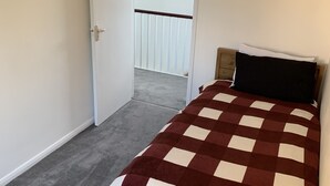 A bedroom with a checkered bedspread, a wooden headboard, and a door leading to a balcony. - 5 Bedroom House (Upminster)