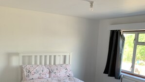A bedroom with a white bed, floral bedding, a radiator, and a window with curtains. - 5 Bedroom House (Upminster)