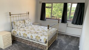 A bedroom with a bed, bedside tables, a radiator, and a window with curtains. - 5 Bedroom House (Upminster)