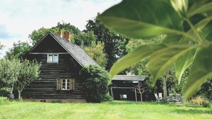 Un chalet rustique en rondins de bois, doté d’une cheminée, entouré d’une végétation luxuriante et d’arbres.