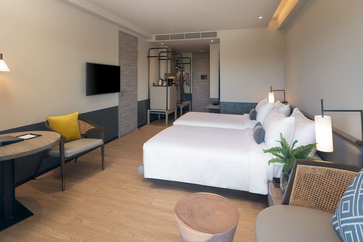 A modern hotel room with a large bed, a desk with a chair, a TV, and a small table.