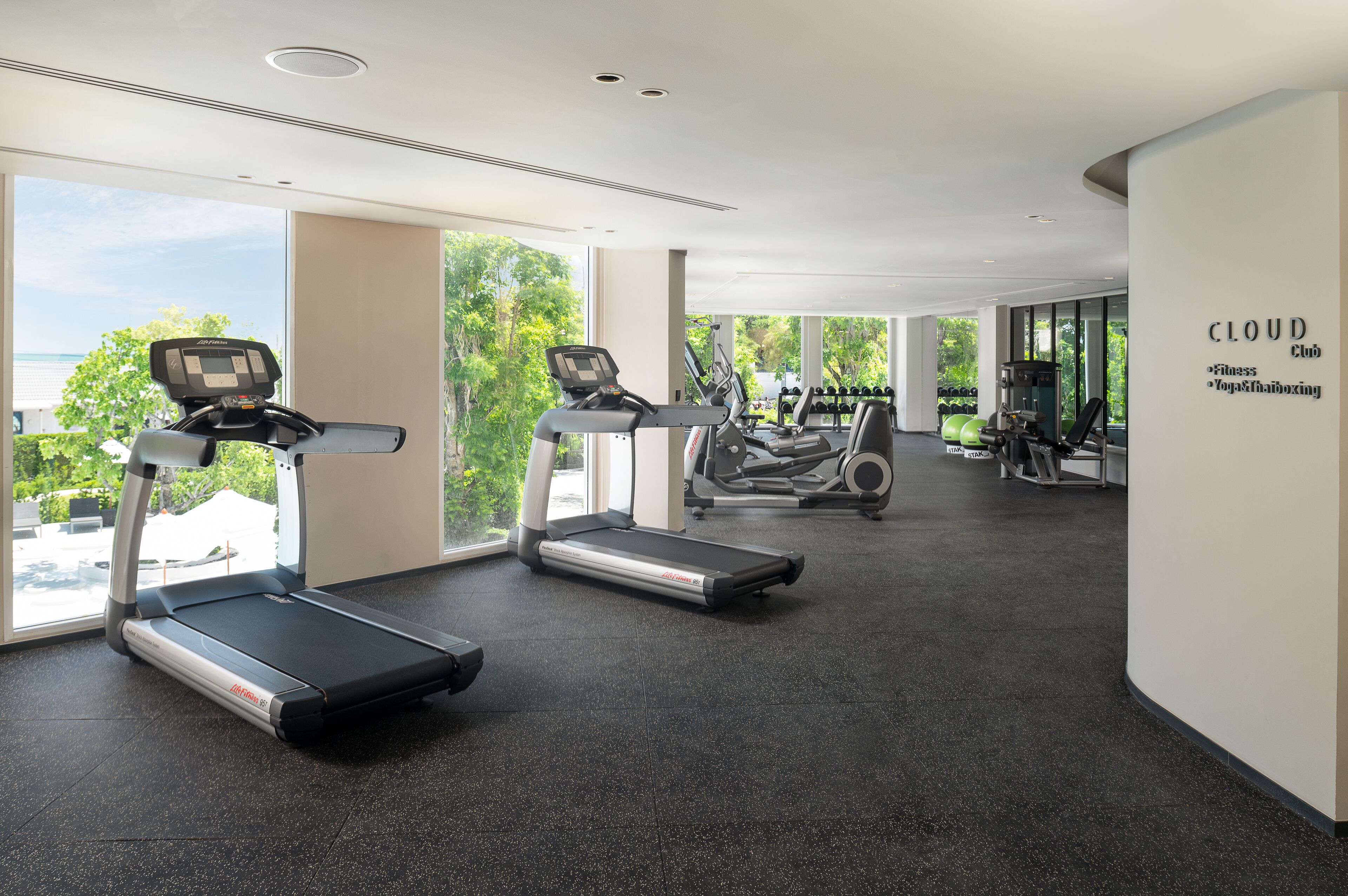 Un gimnasio moderno con cintas de correr, máquinas de pesas y un amplio ventanal con vistas al exterior.