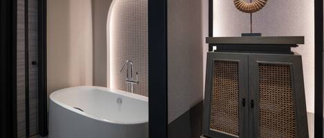 A modern bathroom with a freestanding bathtub, a wall-mounted mirror, and a cabinet with a perforated design.