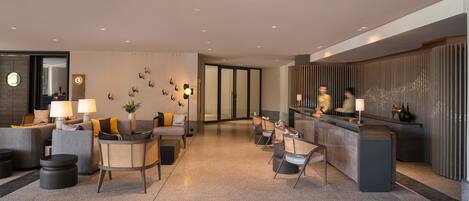 A modern lobby with a reception desk, seating area, and a wall-mounted clock.