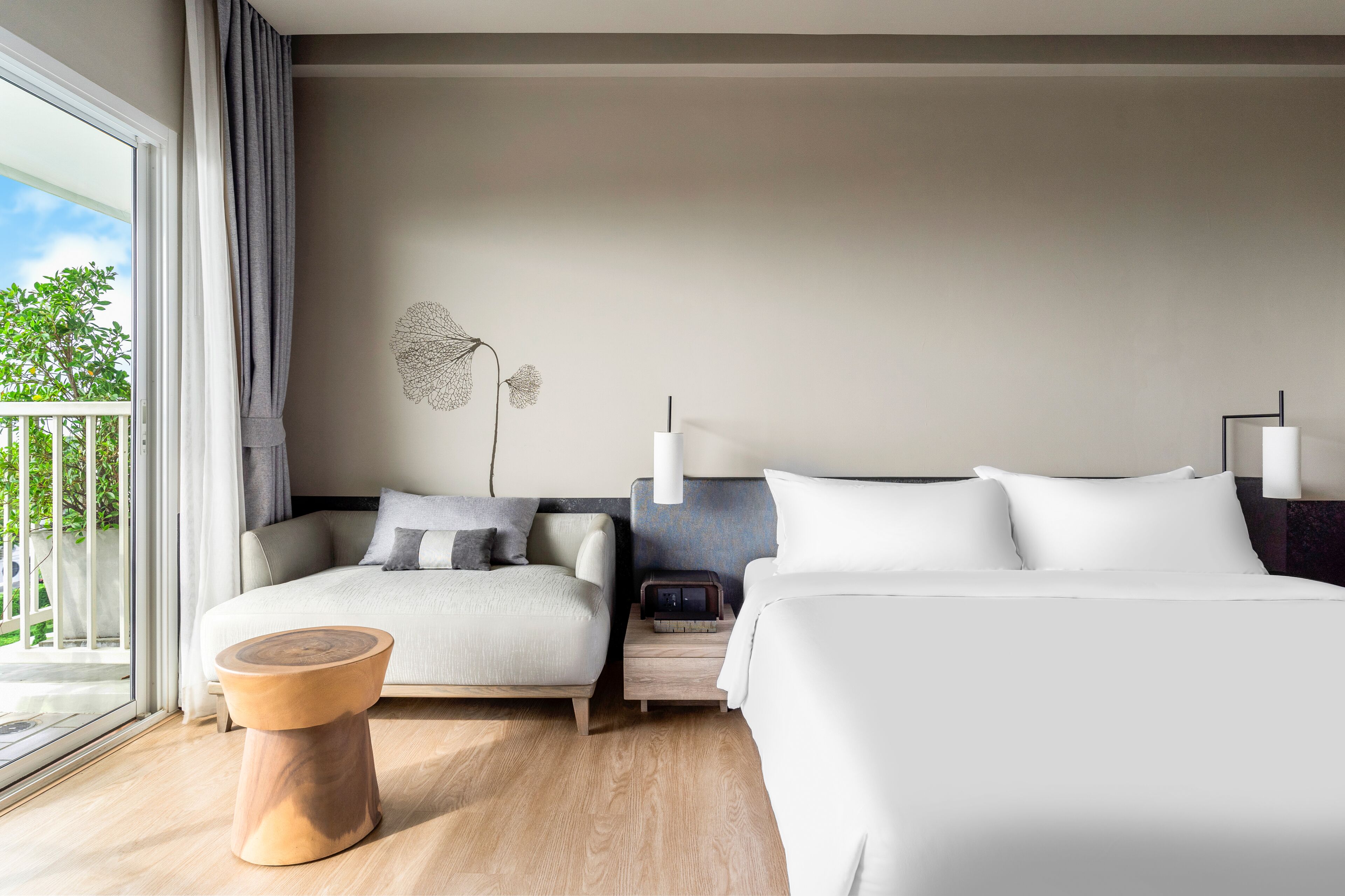 Une chambre d’hôtel moderne avec un grand lit, un canapé, une petite table d’appoint en bois, une table de chevet avec une radio et un élément décoratif mural.