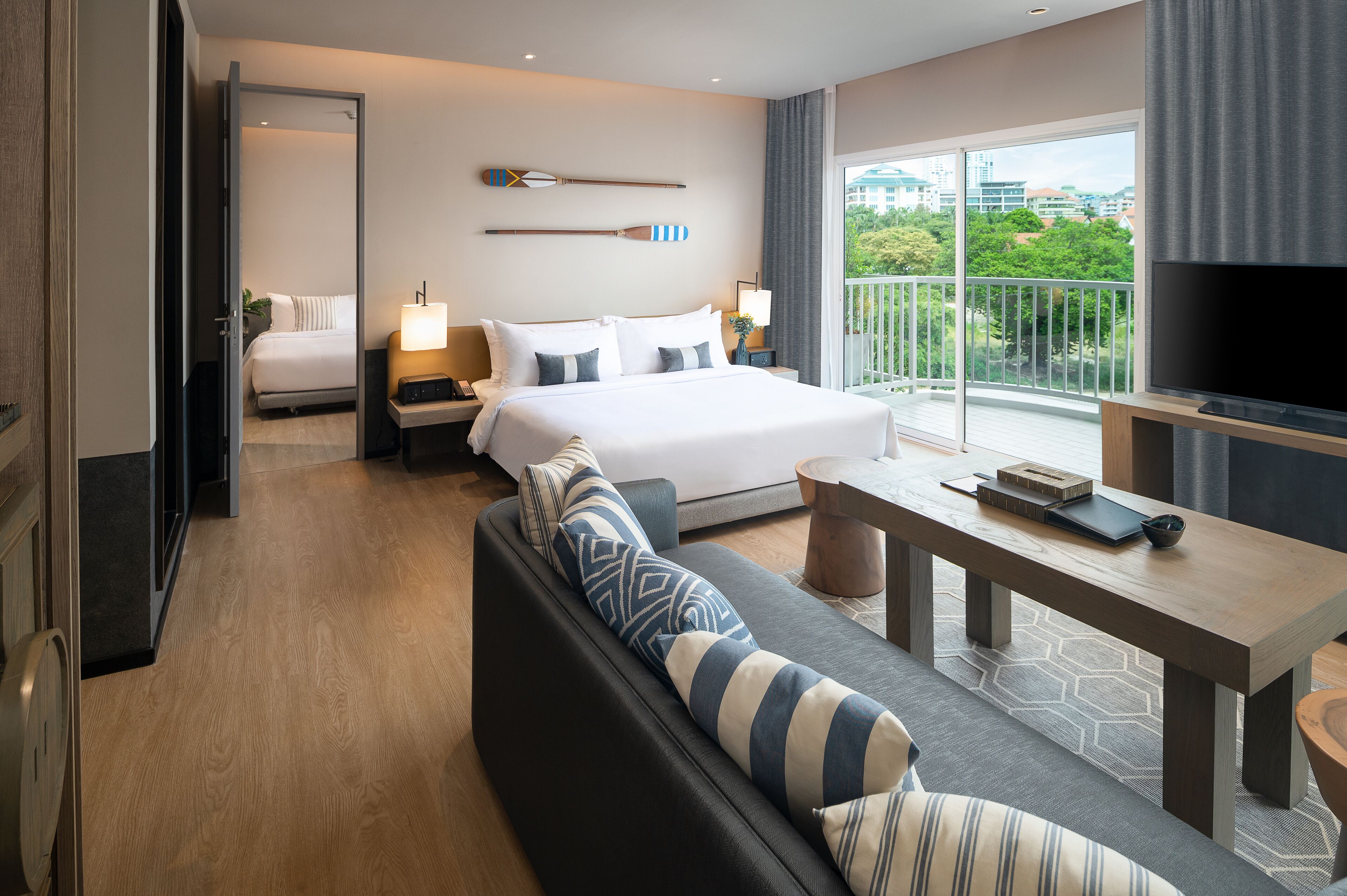 A hotel room with a bed, a sofa, a TV, and a balcony with a view.