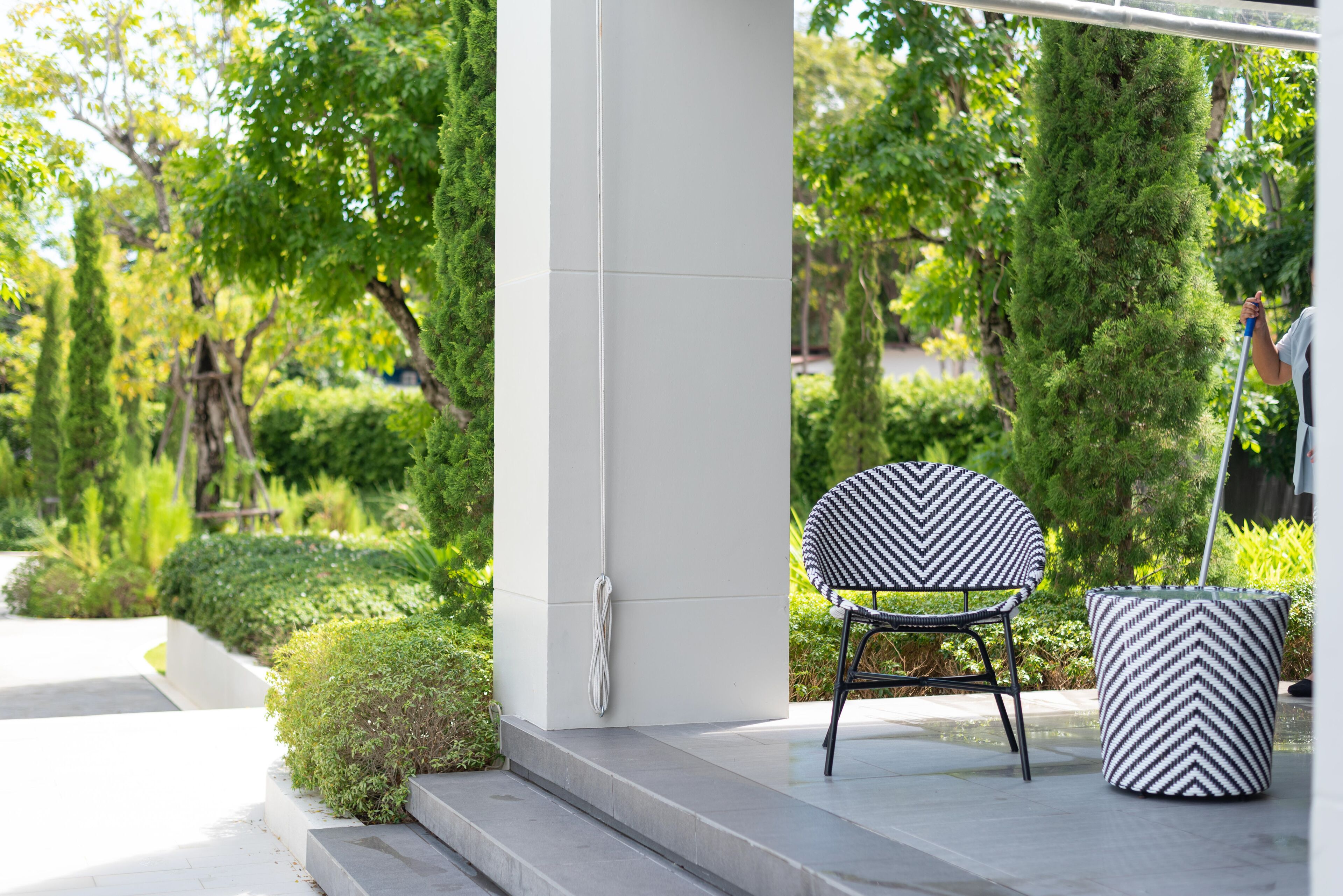 A modern outdoor seating area with a chair and a patterned ottoman, surrounded by lush greenery and a white column structure.