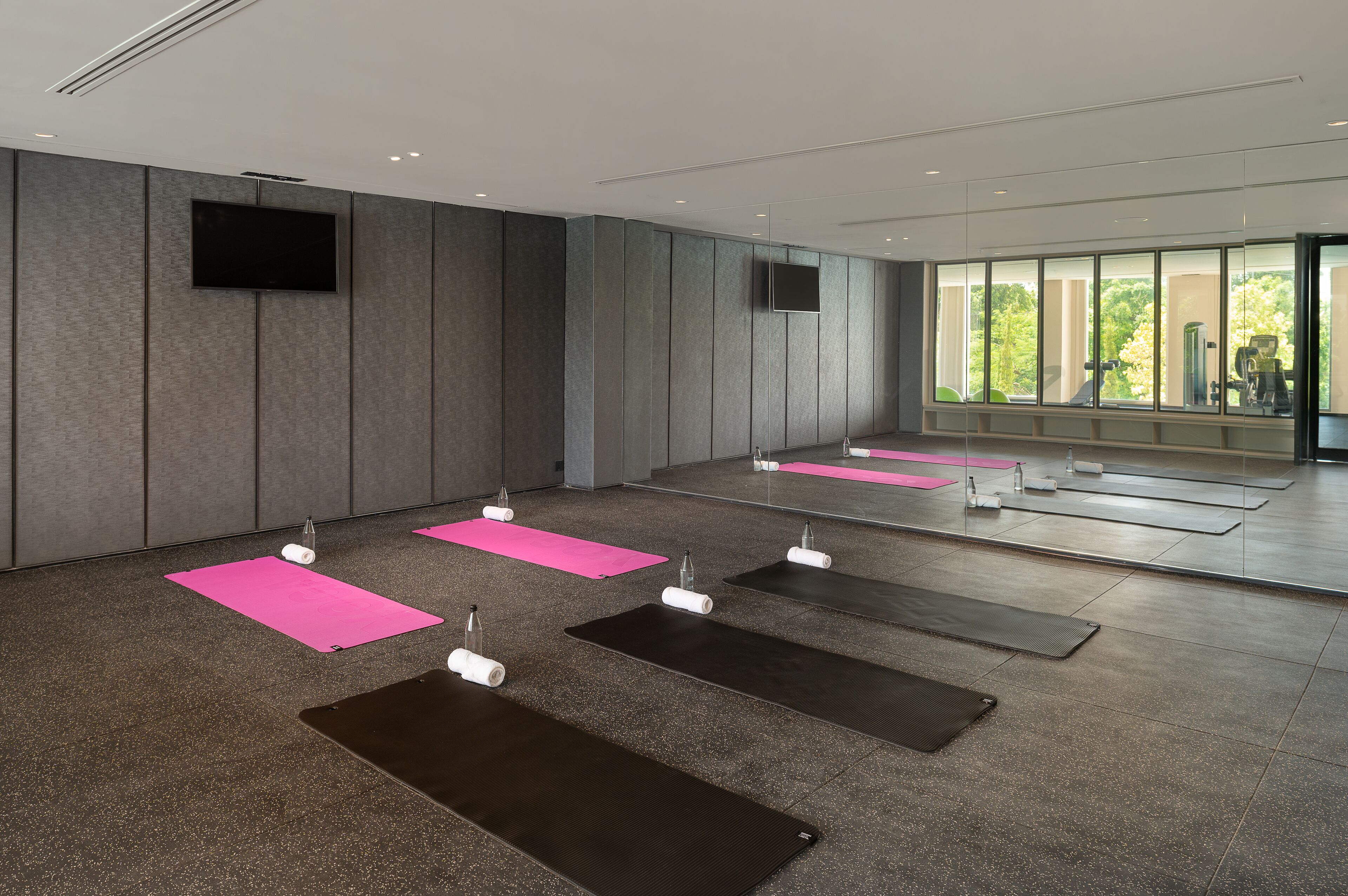 Een moderne fitnessruimte met sportmatten, spiegels en een televisie aan de muur.