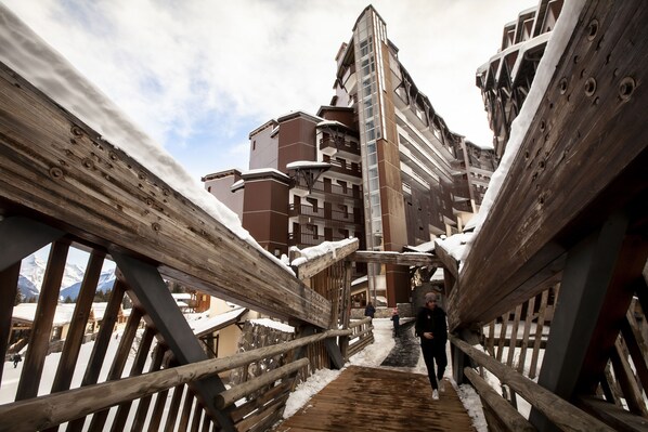 A wooden bridge leading to a building with multiple balconies and a snowy environment.