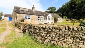 A stone house with a thatched roof, a blue door, and a garden with a stone wall. - Allergarth Barn (Carlisle)