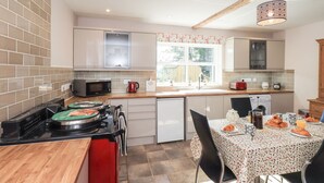 A compact kitchen with a microwave, kettle, and toaster. There's a dining table with chairs and a window providing natural light. - Allergarth Barn (Carlisle)