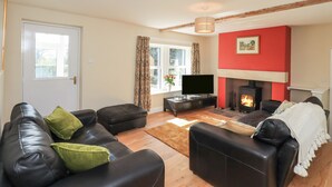 A living room with a fireplace, a television, and a sofa with green cushions. - Allergarth Barn (Carlisle)