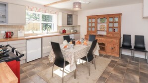 A modern kitchen with a dining area, featuring a wooden cabinet, a red kettle, and a tiled backsplash. - Allergarth Barn (Carlisle)