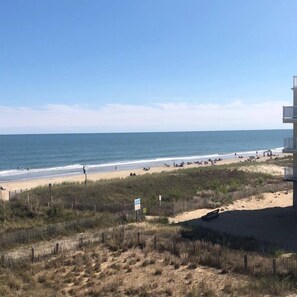 A beach with a fence, a building with a balcony, and the ocean in the background.