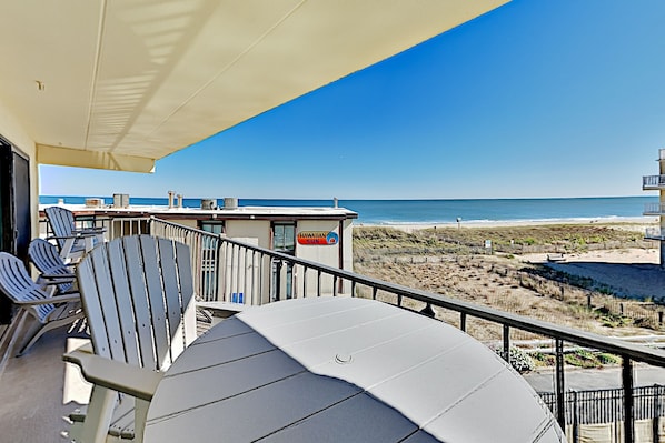 A balcony with a view of the beach, a sign reading "Hawaiian Sun," and several Adirondack chairs.
