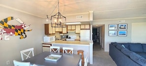 A modern kitchen with white cabinets, a central island, and a dining area with a dark table and white chairs.