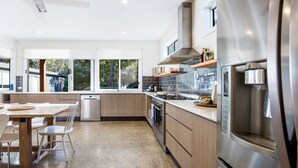 A modern kitchen with a dishwasher, stove, and refrigerator. There is a dining area with a table and chairs. - Ginger's - Pet Friendly - 4 Min Walk to Beach (Callala Beach)