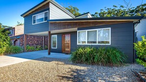 A modern two-story house with a dark exterior, a wooden front door, and a gravel driveway. - Ginger's - Pet Friendly - 4 Min Walk to Beach (Callala Beach)
