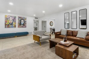 A modern living room with a grey sofa, a brown leather couch, and a coffee table. There are two paintings on the wall and three mirrors.
