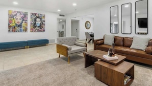 Uma sala de estar moderna com sofá, poltrona, mesa de centro e uma obra de arte na parede.