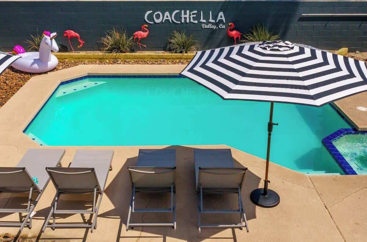 Una piscina con sillas de descanso y una sombrilla a rayas, rodeada de flamencos y un flotador con forma de unicornio.
