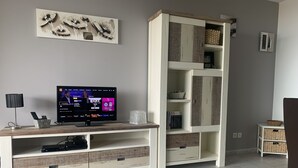 A living room with a TV on a wooden stand, a white cabinet with shelves, and a grey wall. - Apartment T2 Sea View, Air-conditioned, 4 People swimming pool in the residence  (Lumio)