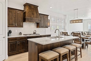 Enjoy cooking in this kitchen with a large island and bar stools, featuring a range hood and modern light fixture.