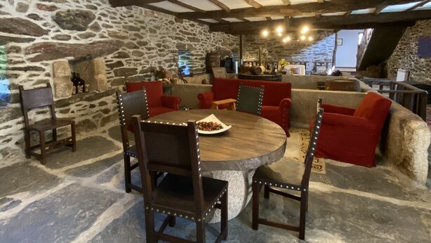 Un comedor rústico con pared de piedra, vigas de madera y una mesa redonda con sillas.