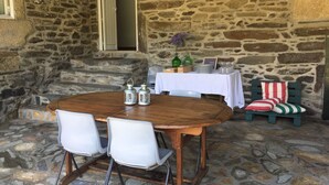 Un área de comedor al aire libre con paredes de piedra, una mesa de madera y sillas blancas.