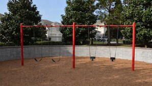 A playground with swings and a brick wall. - IPG Florida Vacation Homes Bella Piazza Resort (Clermont)
