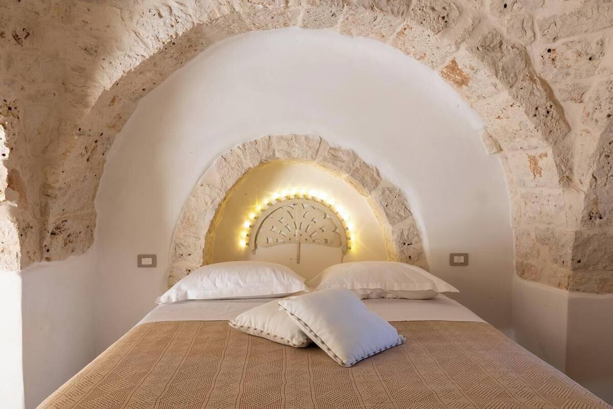A bedroom with a stone arched ceiling, a bed with white bedding, and a headboard with a clock.