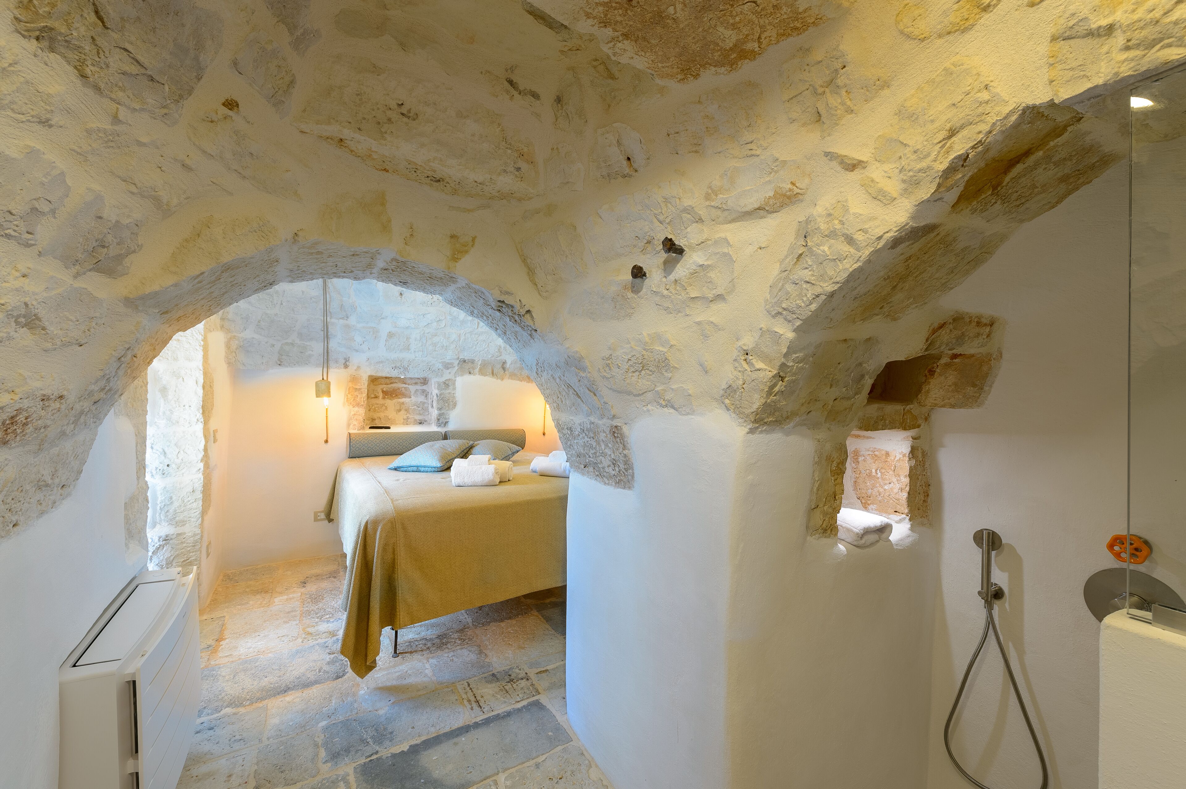 Ein Schlafzimmer mit Steinwänden, einem Bett, einer Hängelampe und einer Dusche.
