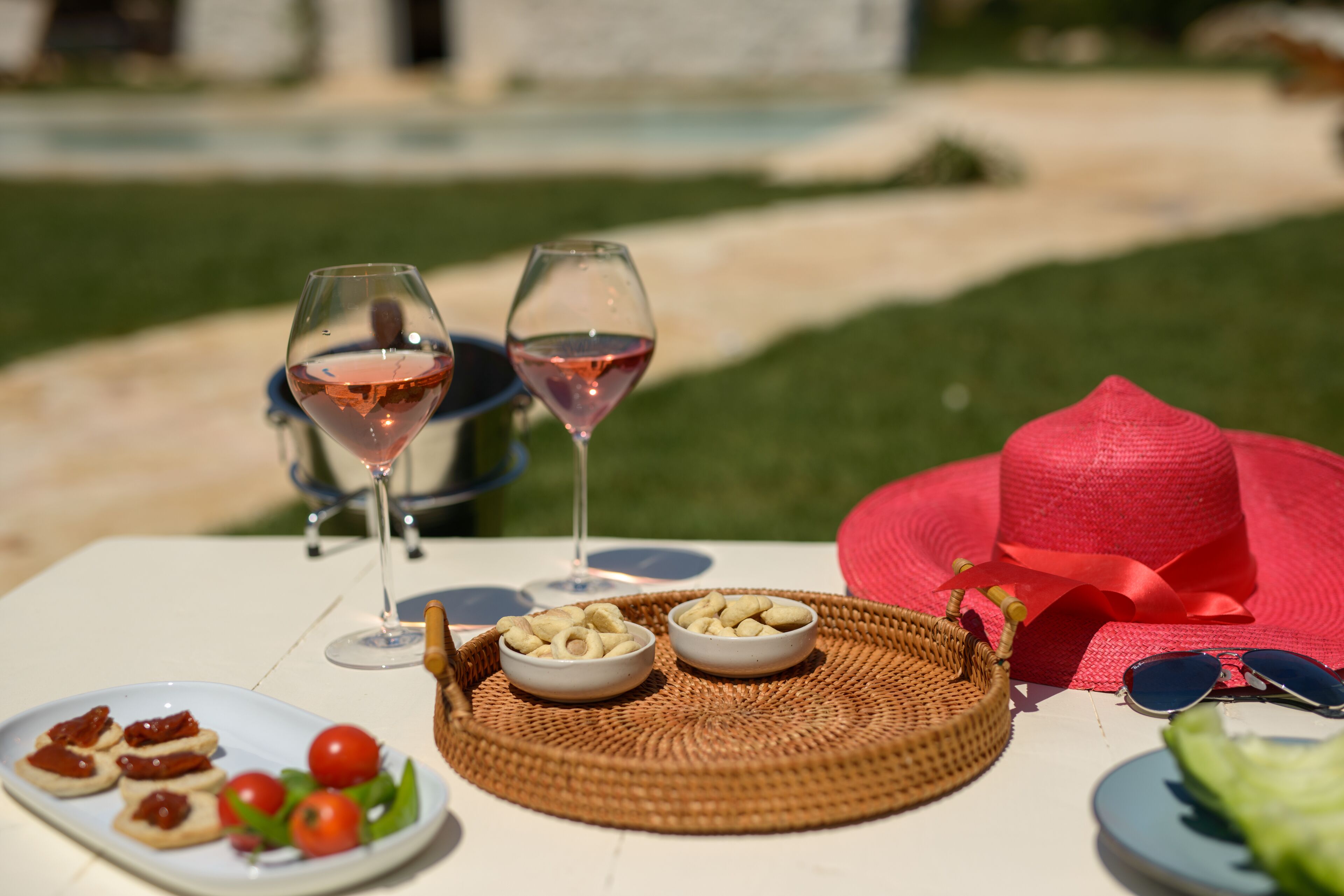 Une table dressée avec deux verres à vin, un chapeau rouge et une assiette contenant de la nourriture, ainsi qu’un panier rempli de collations.