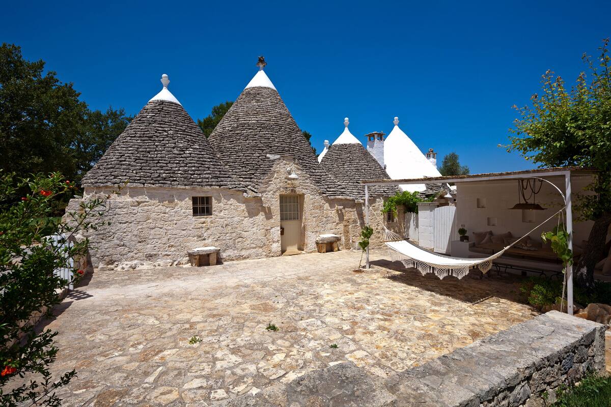 A stone building with multiple conical roofs, a stone courtyard, and a hammock.