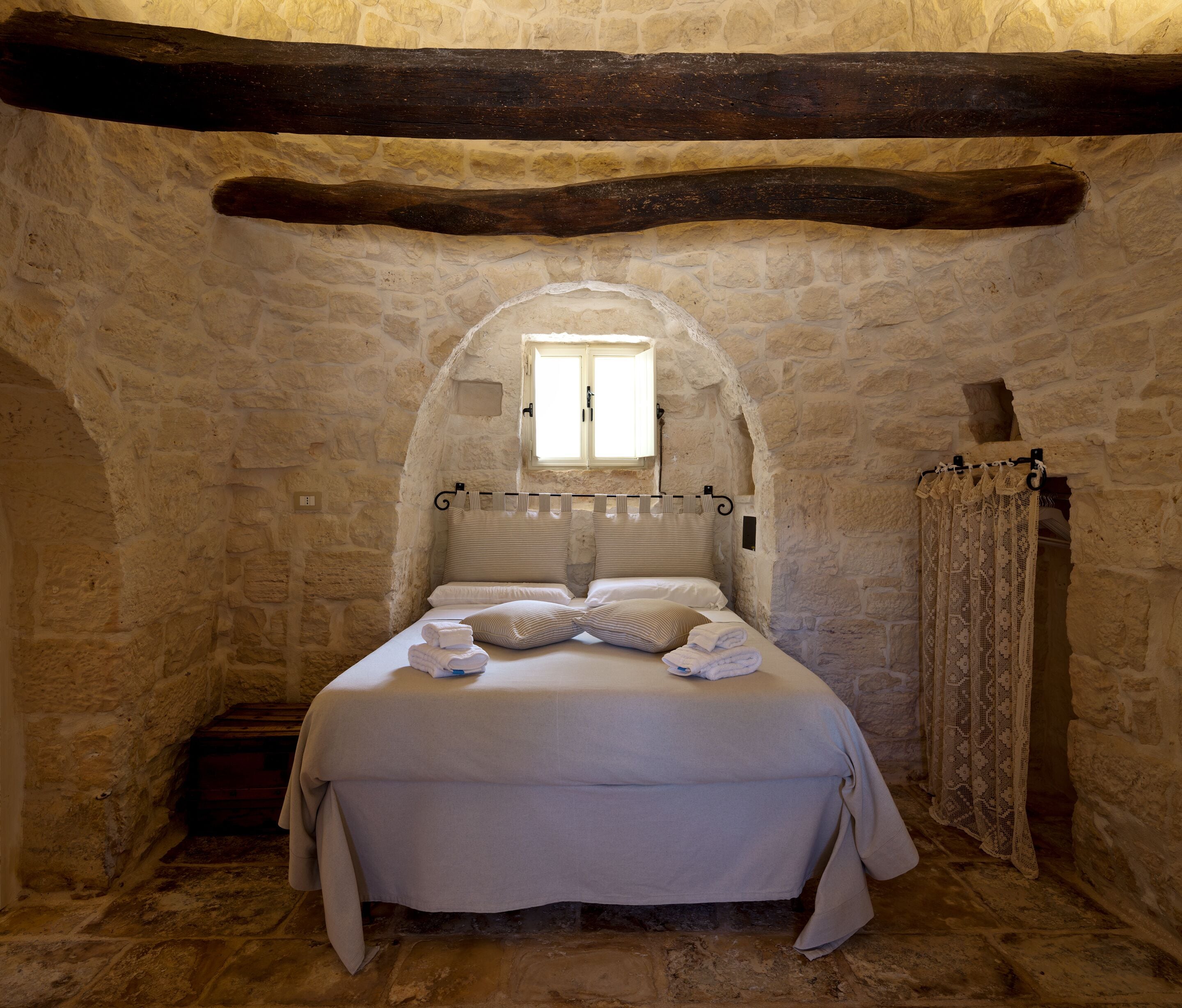 A stone-walled bedroom with a bed, a window, and a curtain.