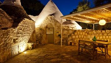 A stone building with a conical roof, a covered outdoor seating area, and a table with chairs.