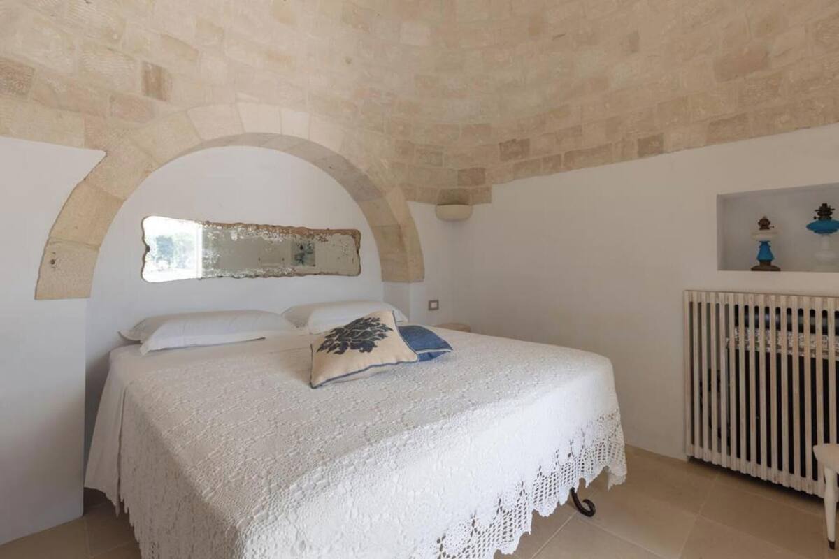 A bedroom with a white bed, a small arched window, and a white radiator.