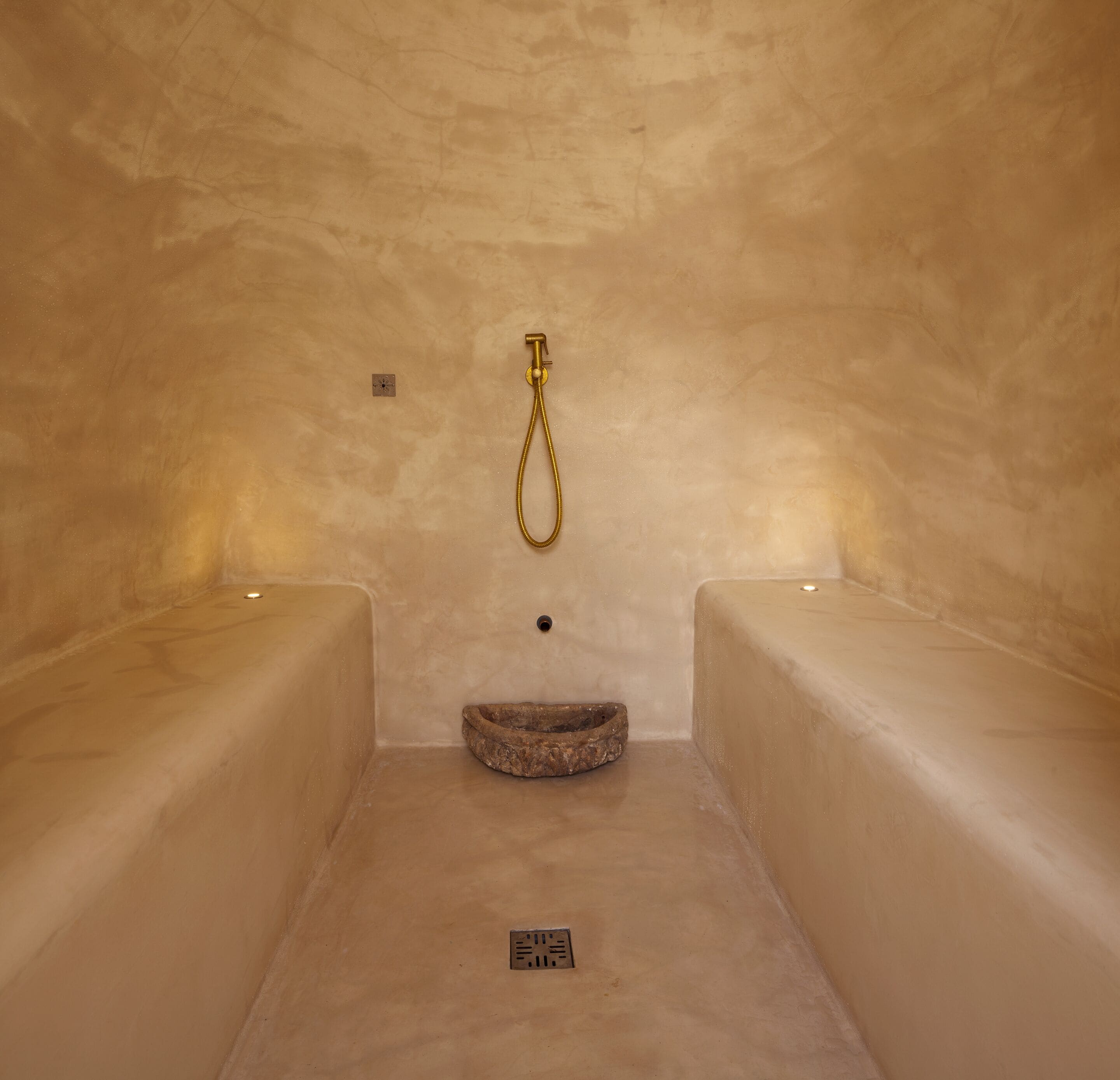 Een spa ruimte met twee banken, een gouden douchekop en een stenen wasbak.
